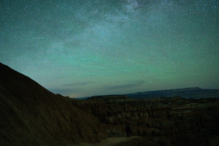 Starry night sky over desert landscape with silhouetted hills.
