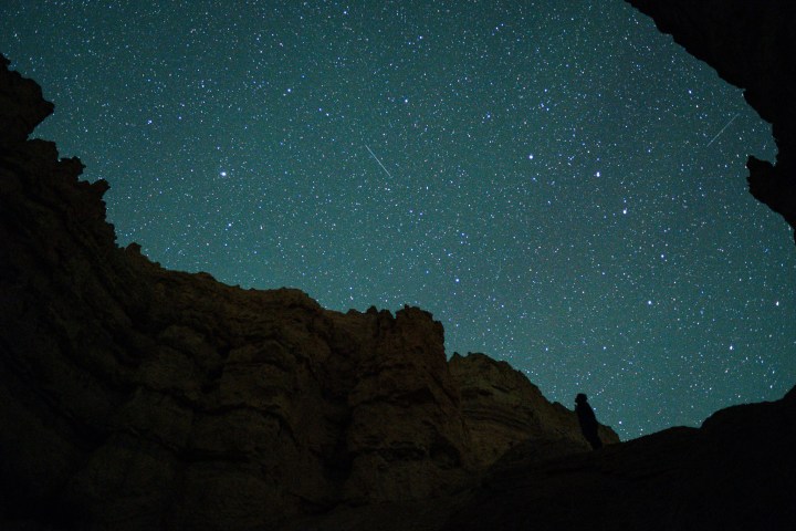 Starry night sky with silhouette of rock formations and lone figure.
