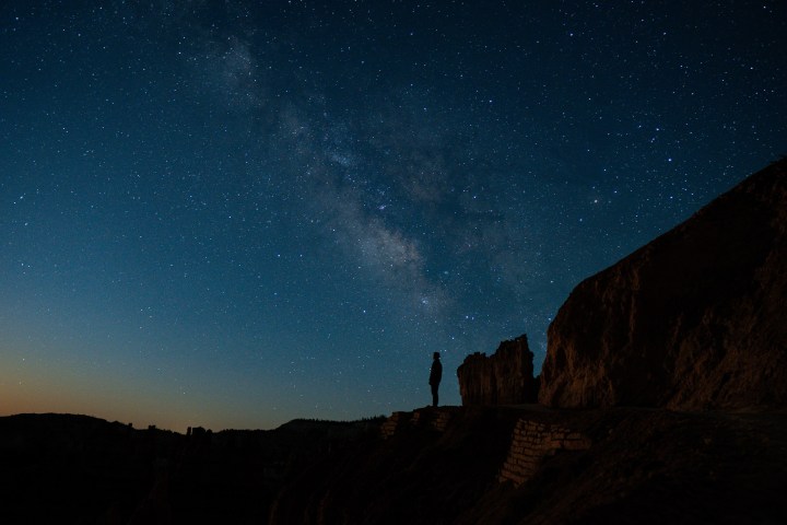 Silhouette of person on cliff under starry night sky with Milky Way.