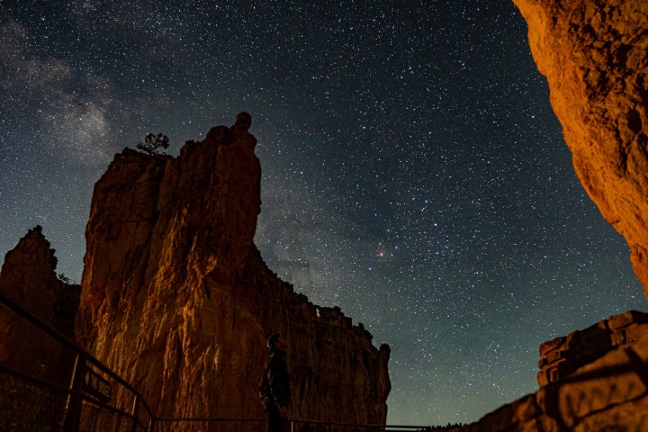 Starry night sky over rocky formations with a person in silhouette.
