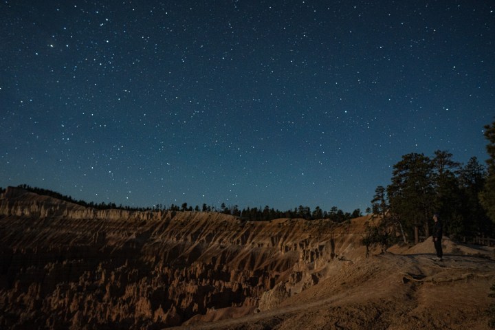Night sky with stars over a canyon and trees.